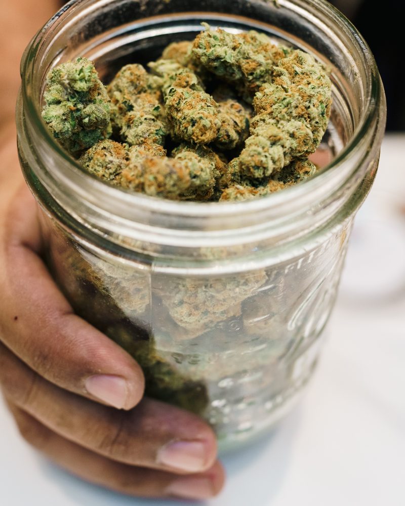 Glass-jar cured cannabis flower at the counter of Coffeeshop The Mantis, Ao Nang